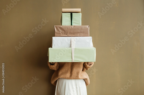 Young beautiful woman hold paper gift boxes stack against olive wall. Festive Christmas / New Year holidays celebration concept. photo