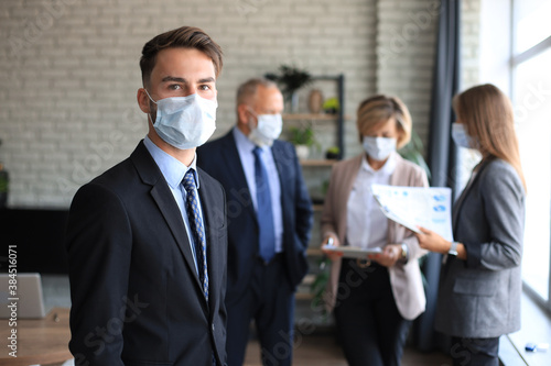 Businessman in medical mask with colleagues in the background in office.