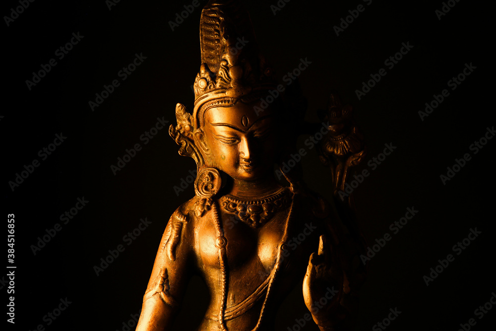 Fototapeta premium Close up of isolated illuminated hindu Shiva god golden bronze statue with raised hand on blank black background