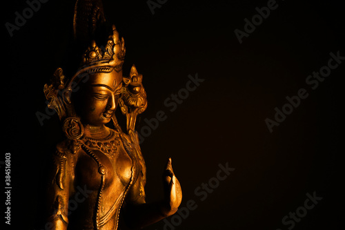 Close up of isolated illuminated hindu Shiva god golden bronze statue with raised hand on blank black background