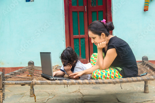 Indian rural mother teaching daughter online on laptop using internet. photo