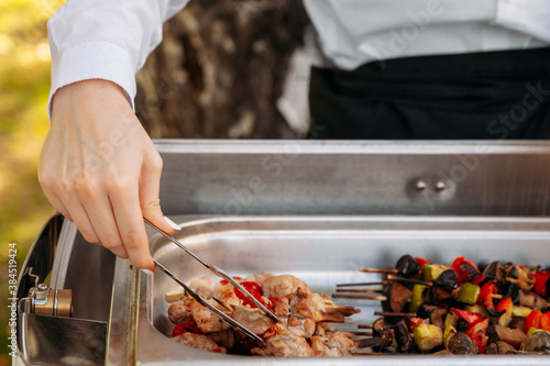Outdoor catering banquet in summer. Waiter in white shirt puts a barbeque from a chafing dish on a plate. The waiter serves guests at the banquet