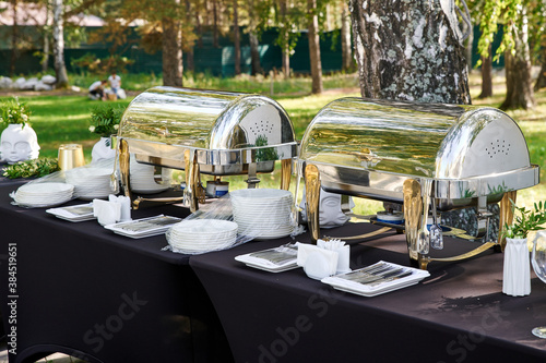 Outdoor catering banquet in summer. Banquet table with chafing dish, plates and cutlery photo