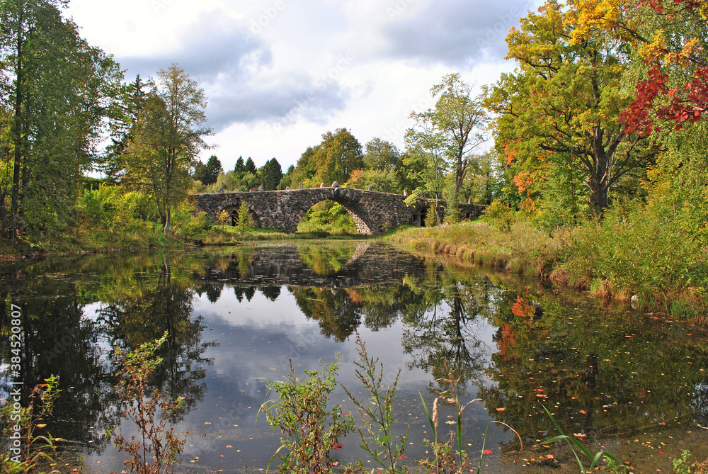 Autumn day in the old park. Pond and old stone bridge