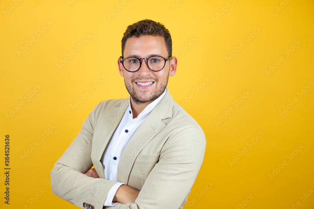 Young handsome businessman wearing suit over isolated yellow background smiling with her arms crossed Young handsome businessman wearing suit over isolated yellow background smiling with her arms crossed