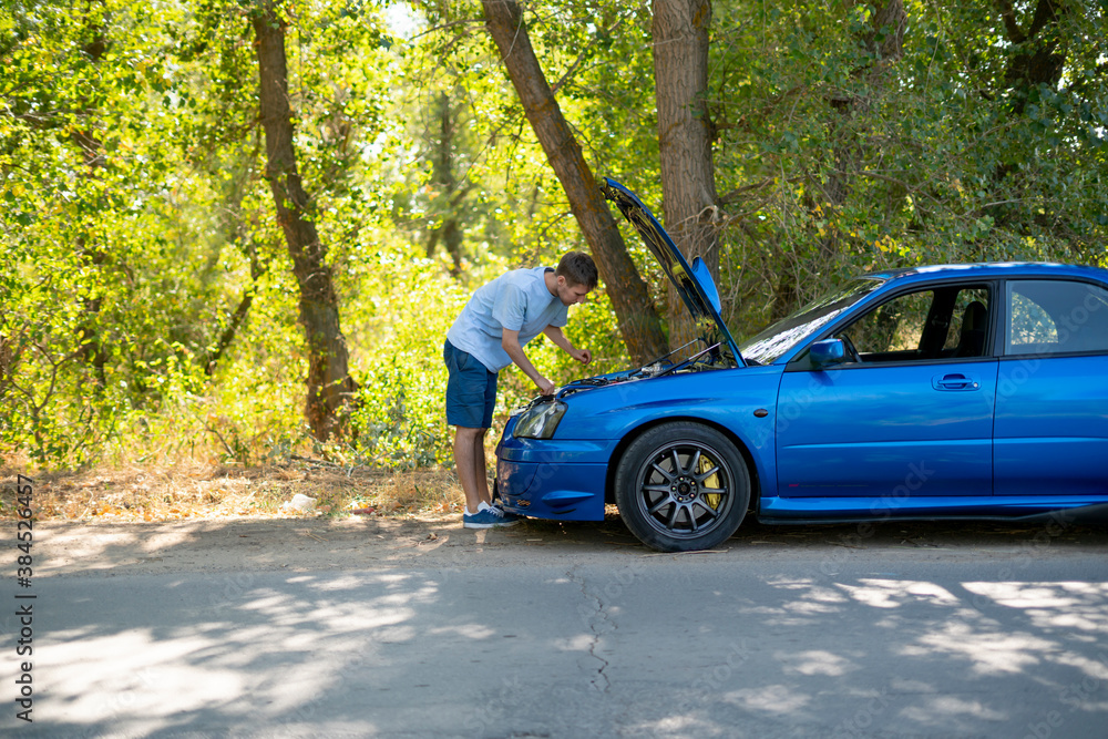 young man standing near the car with opened hood and fix some problems with engine young man standing near the car with opened hood and fix some problems with engine