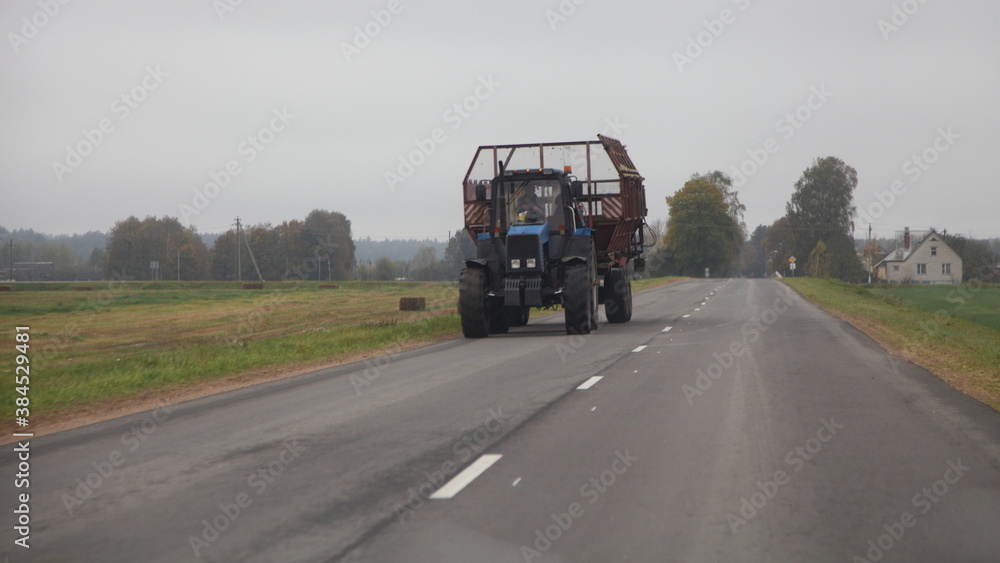 Old Russian wheeled tractor with empty hay trailer move on the rural empty asphalt road at autumn day for loading, front view, agribusiness farming equipment