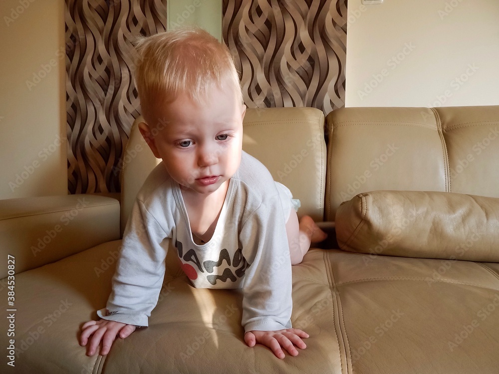 blond little boy on a beige couch looks intently away, cute toddler in home clothes blond little boy on a beige couch looks intently away, cute toddler in home clothes