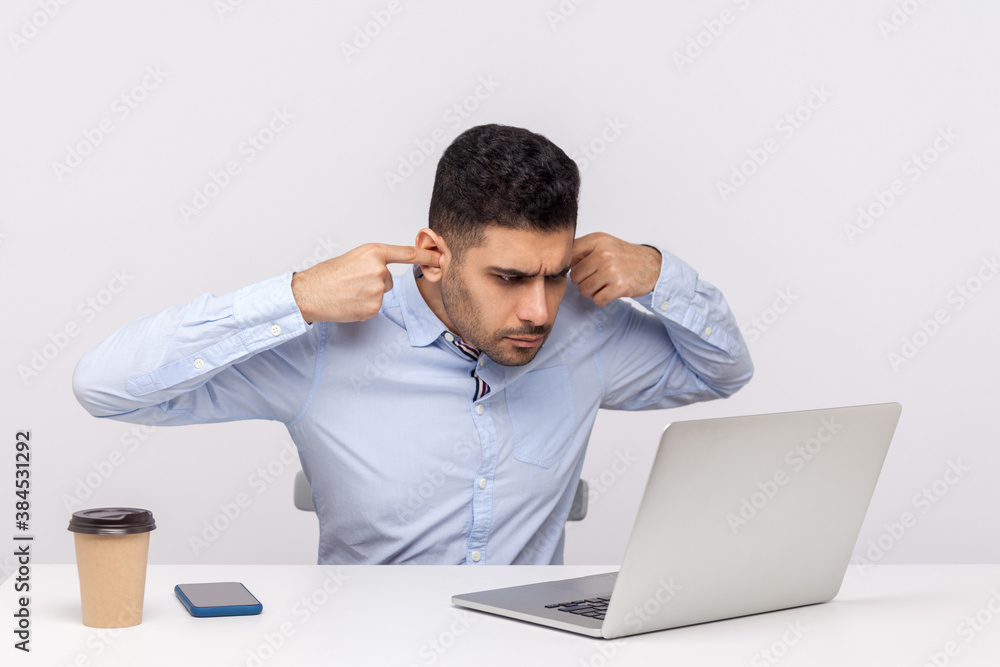 Don't want to hear you! Irritated businessman sitting office workplace, closing ears while talking video call on laptop, looking annoyed by unpleasant job conference online. studio shot isolated Don't want to hear you! Irritated businessman sitting office workplace, closing ears while talking video call on laptop, looking annoyed by unpleasant job conference online. studio shot isolated