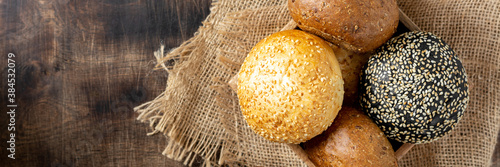 Sesame buns for burgers. Buns in a wooden box on a brown wooden table. Homemade buns with sesame seeds. Top view with space for text. Copyspace. Banner	