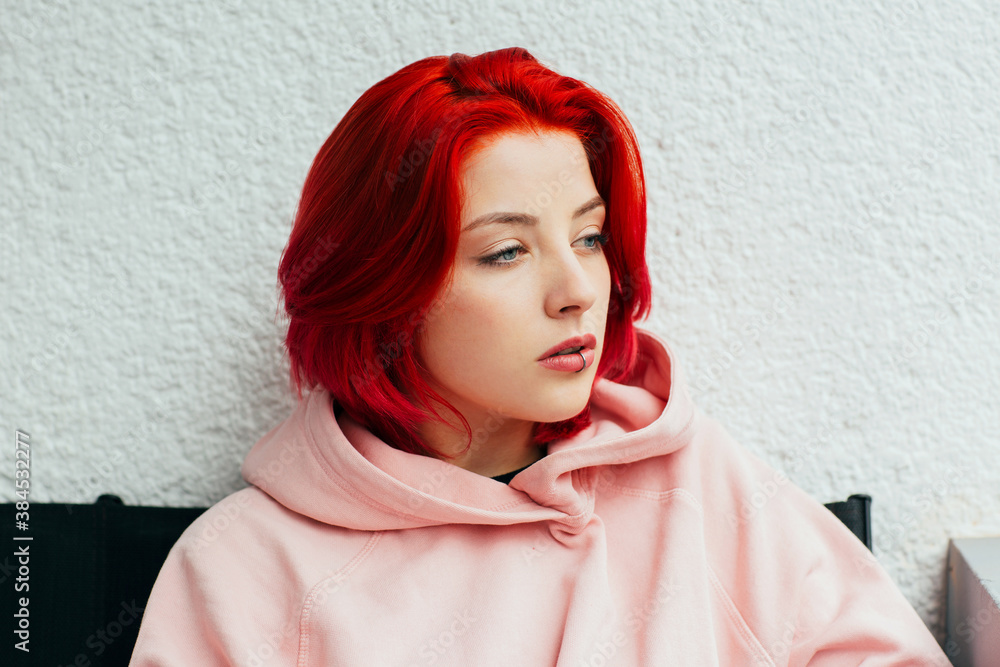 Portrait of a cool teen girl with bright red hair, lip piercing and pink  hoodie looking to side thinking Stock Photo | Adobe Stock
