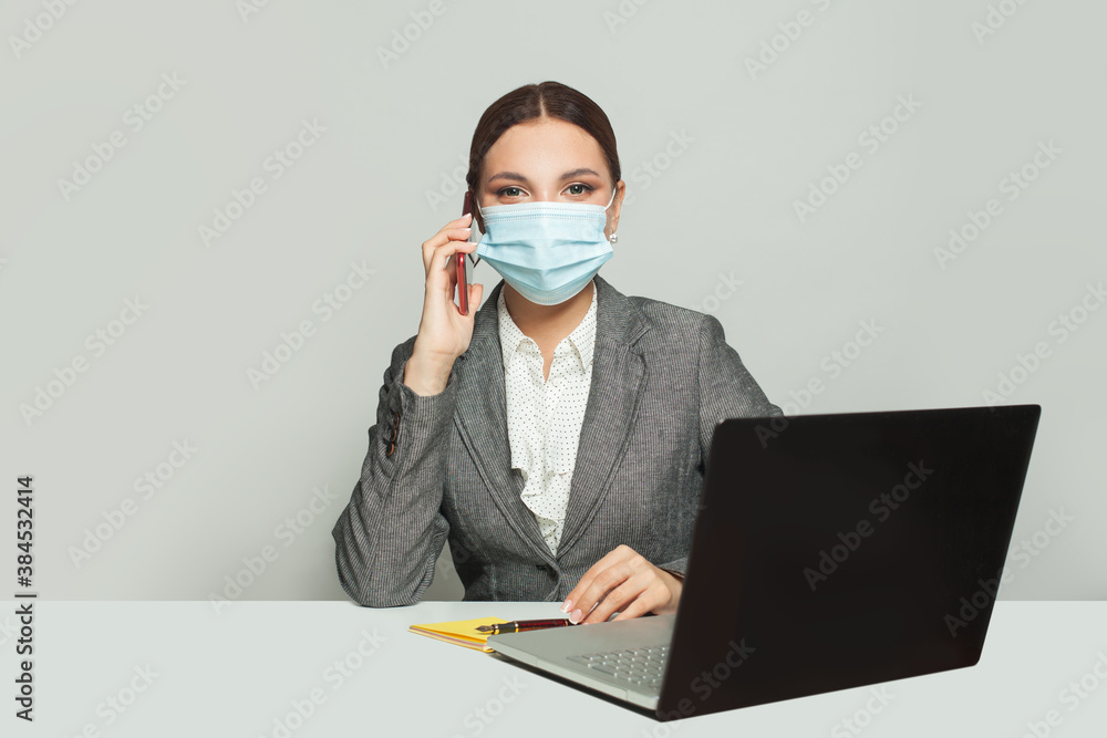 Happy smart business woman in protective medical mask with phone and laptop working in office Happy smart business woman in protective medical mask with phone and laptop working in office