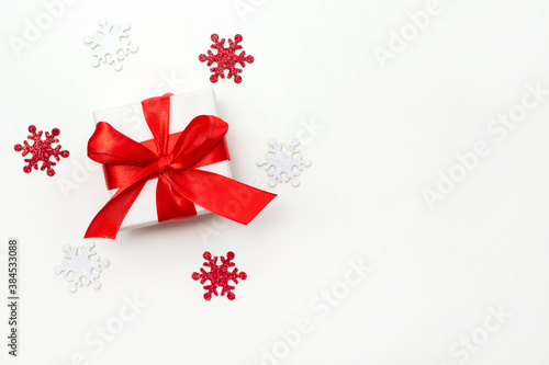 Christmas gift box with red ribbon on a white background with shining snowflakes. Flat lay. Copyspace