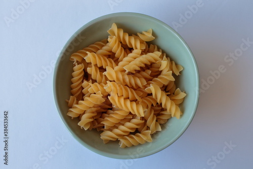 Raw fusilli pasta in a ceramic green plate on a white table. Top view.