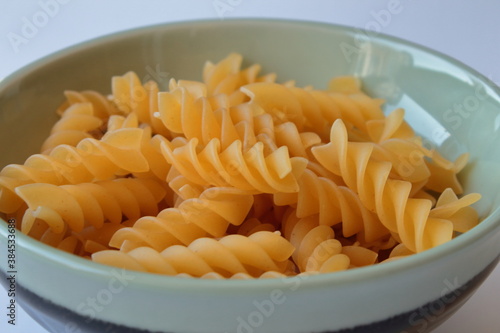 Raw uncooked pasta fusulli in ceramic bowl over white background