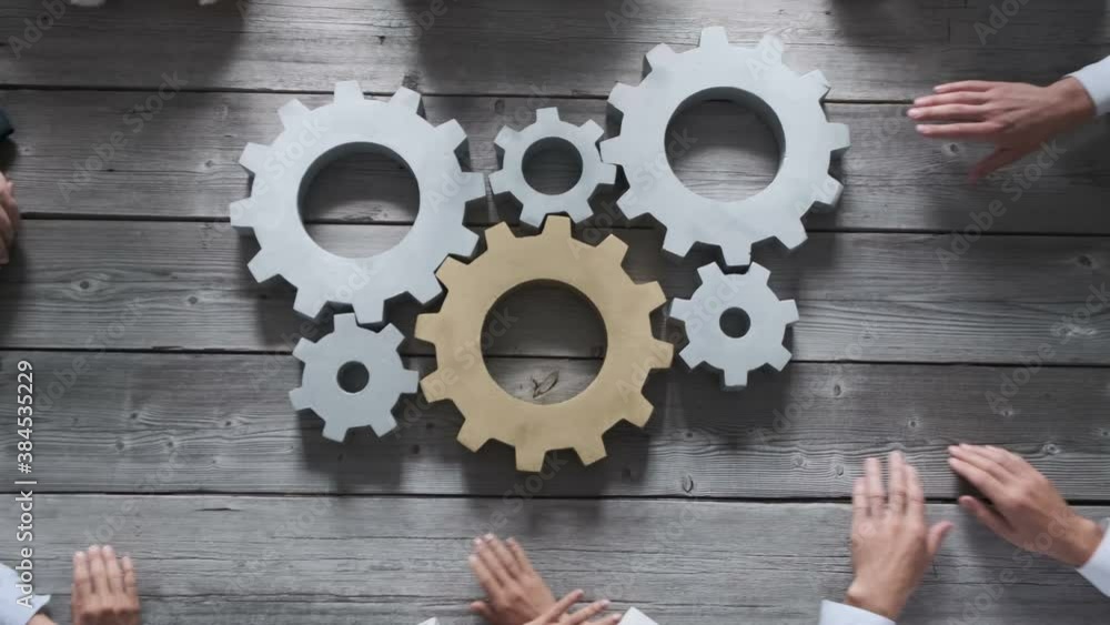 Group of business people joining together silver and golden colored gears on table at workplace teamwork concept