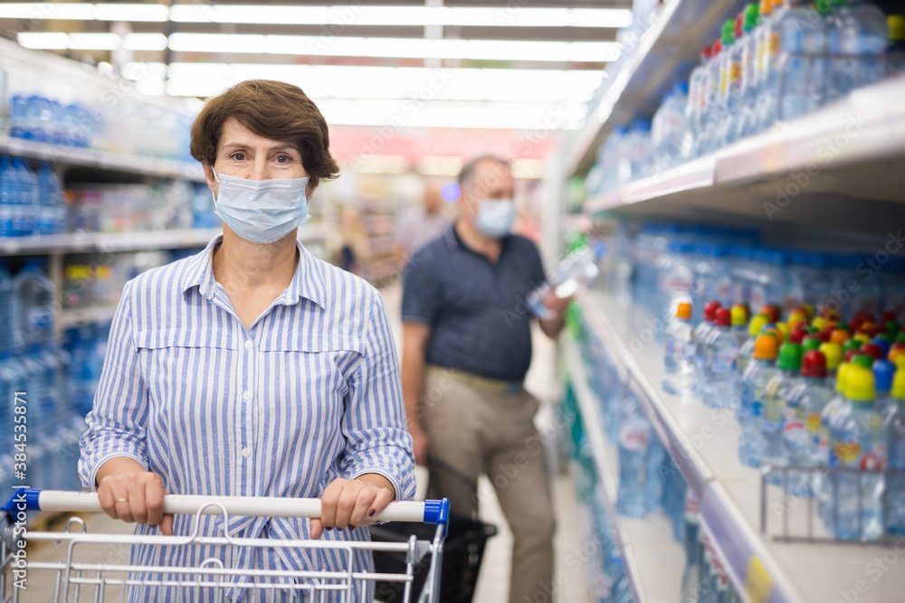Woman wearing protective mask buys water bottles at supermarket
