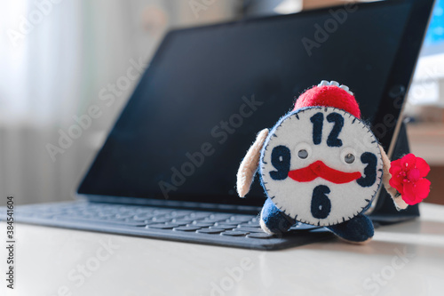 Toy felt handmade cute alarm clock against the background of a black laptop. Concept of online, homeschooling, back to school. Copy space.