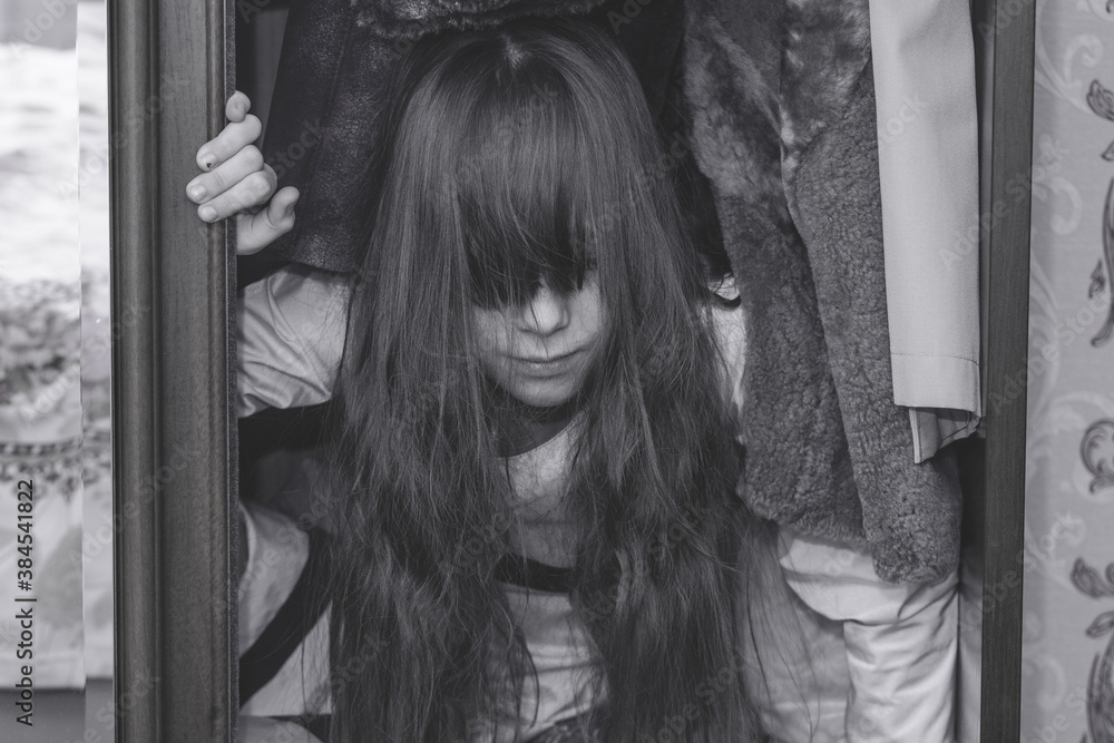 Mad scary girl in cupboard at dark night. Horror background with child possessed by devil. Demon possessed little girl in closet at night. Ghost of little girl at dark night. Child ghost in cupboard. Mad scary girl in cupboard at dark night. Horror background with child possessed by devil. Demon possessed little girl in closet at night. Ghost of little girl at dark night. Child ghost in cupboard.