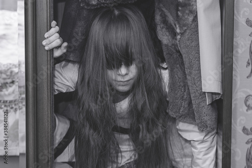Mad scary girl in cupboard at dark night. Horror background with child possessed by devil. Demon possessed little girl in closet at night. Ghost of little girl at dark night. Child ghost in cupboard.