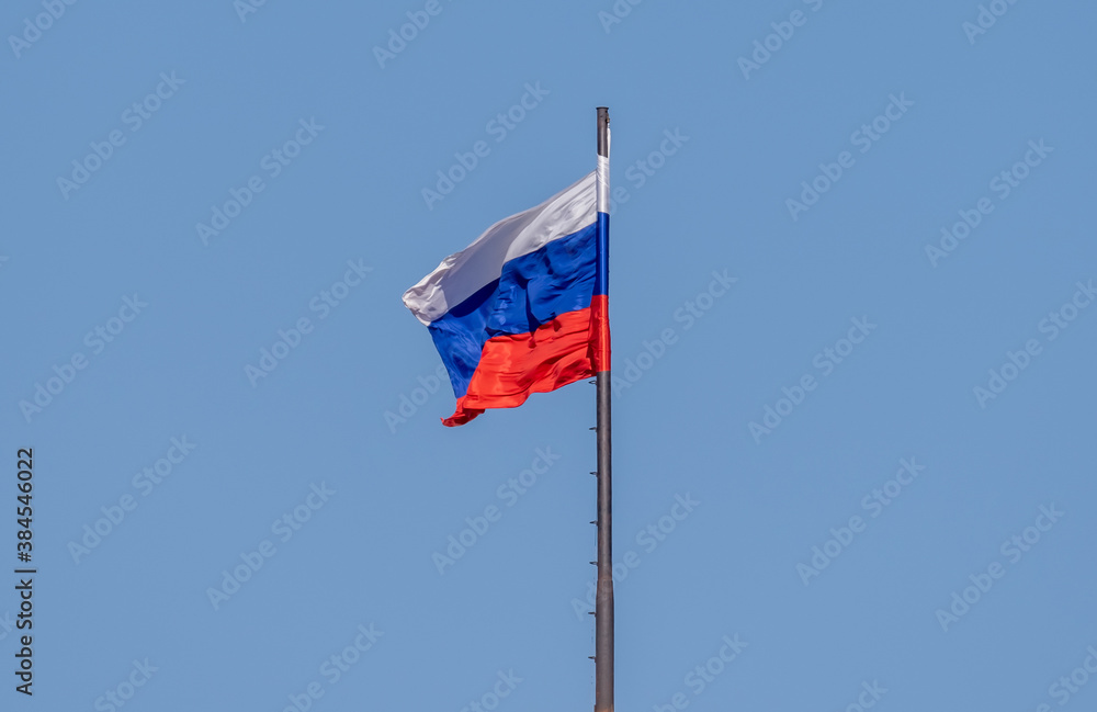 the Russian flag on the flagpole flutters in the wind against the blue sky