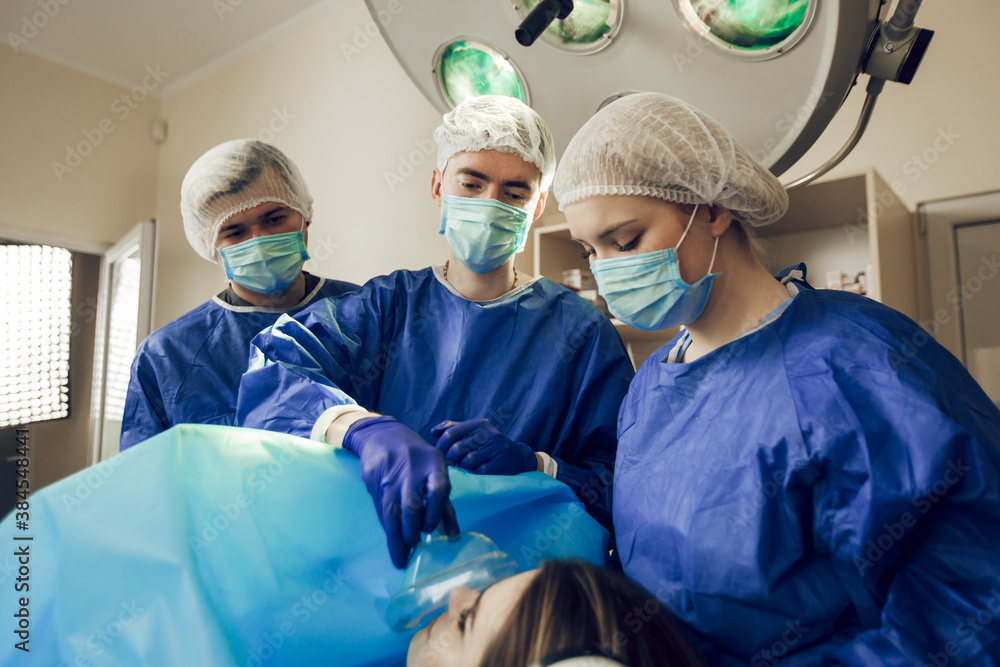 Anesthesia of the patient before operation. Three surgeons at work. Doctors are preparing for surgery. Surgeons and a patient in the hospital Anesthesia of the patient before operation. Three surgeons at work. Doctors are preparing for surgery. Surgeons and a patient in the hospital