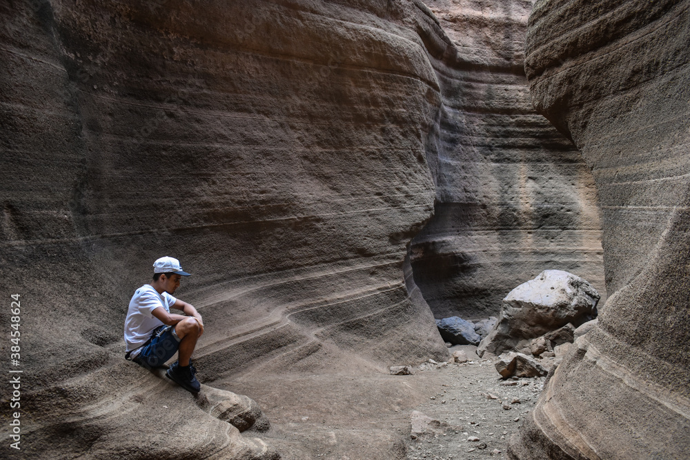 Naklejka premium Young man sitting on some smooth and colorful volcanic stones, Tobas de Colores, Barranco de las Vacas.