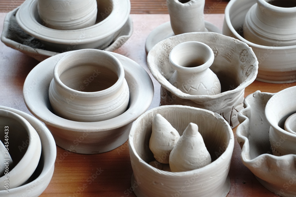 handmade unbacked crockery and pots on the table in the potter's studio. clay before firing in a ceramic kiln handmade unbacked crockery and pots on the table in the potter's studio. clay before firing in a ceramic kiln