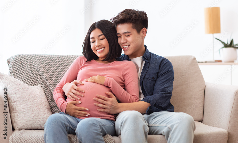 Happy Asian Husband Hugging Pregnant Wife Sitting Together At Home Happy Asian Husband Hugging Pregnant Wife Sitting Together At Home