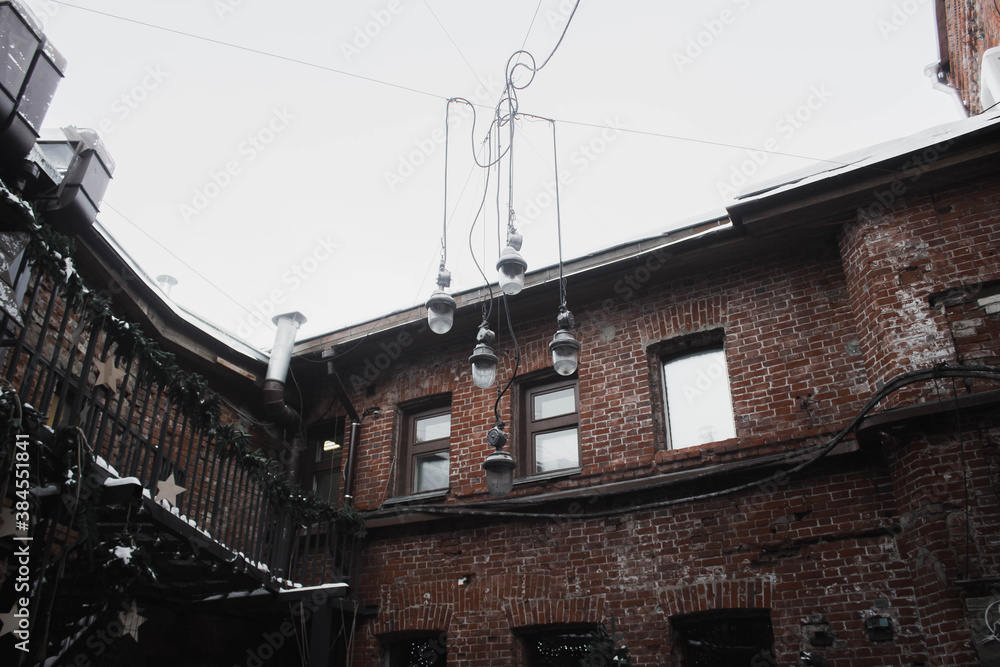 Vintage old building of red bricks with windows, lamps, christmas decorations in city. Old grunge walls. Street architecture at winter. Architectural exterior details. Stock photo