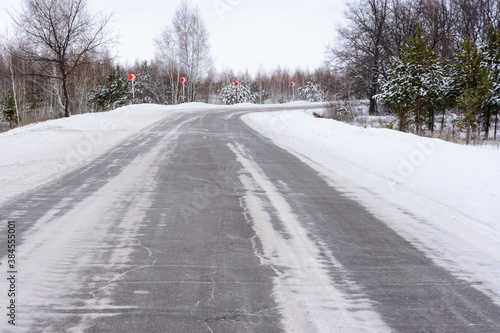 Patterns on the winter highway in the form of four straight lines. Snowy road on the background of snow-covered forest. Winter landscape.