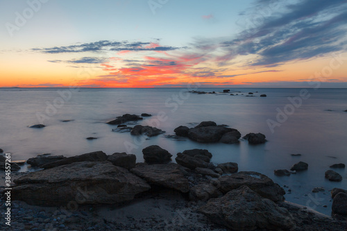 Twilight sunset over rocky shore of Baltic sea. Almost clear sky and orange strap along the horison. Estonia.
