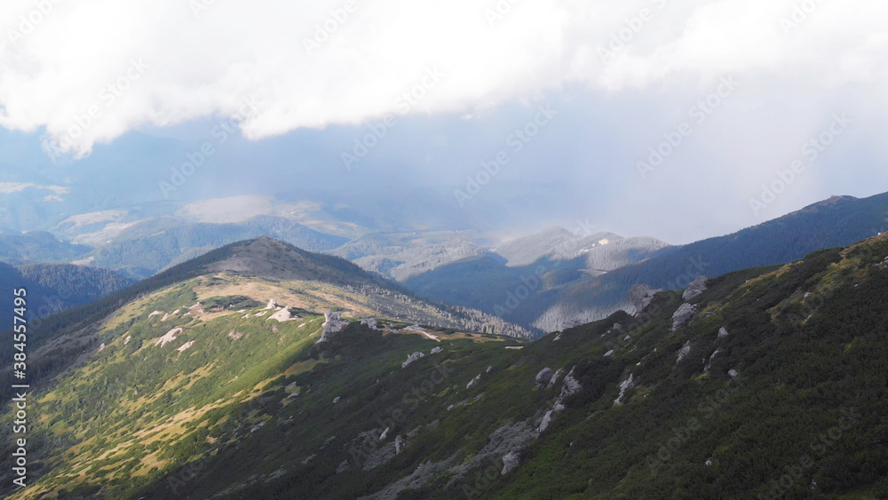 The bright sun illuminates green mountain hills. White cloud of fog is high above the mountains. The bright sun illuminates green mountain hills. White cloud of fog is high above the mountains.