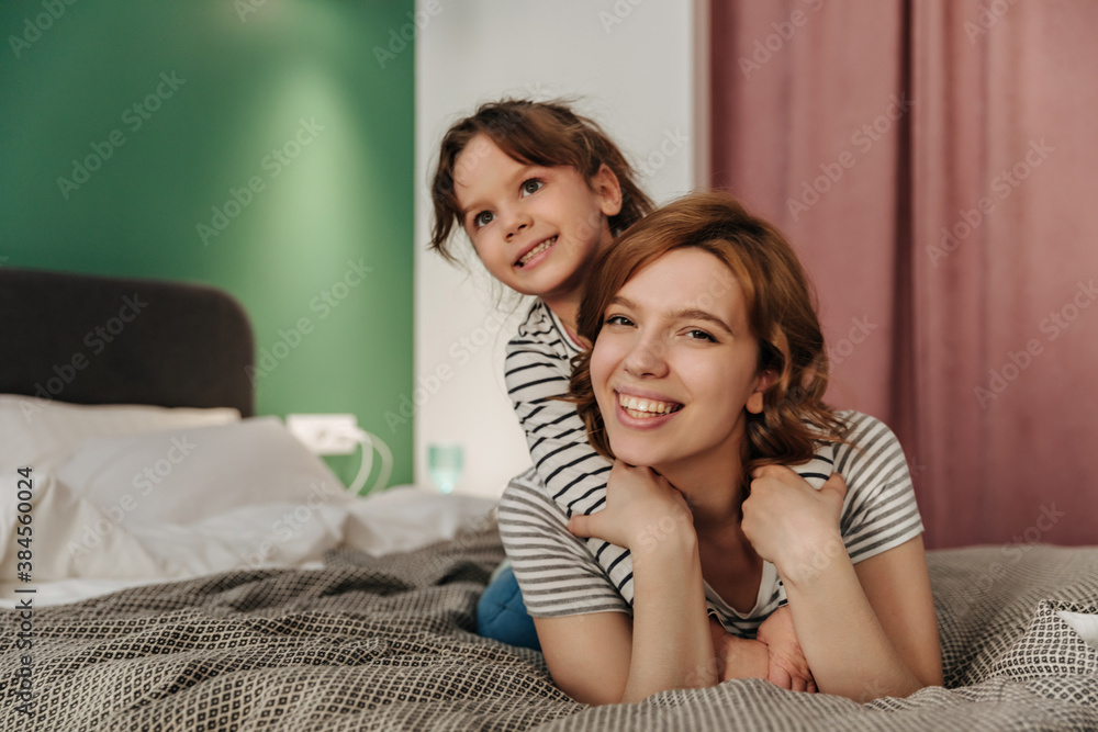 Positive mom and daughter having fun, hugging and lying on bed Positive mom and daughter having fun, hugging and lying on bed