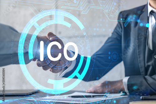 Double exposure of two businesspeople handshake and initial coin offering, ICO hologram drawing background. Concept of partnership in blockchain and cryptocurrency business. Formal wear.