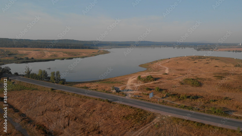 Top view of beautiful lake. Bus station near the asphalt road. Endless plain and mountain hills on the horizon. Top view of beautiful lake. Bus station near the asphalt road. Endless plain and mountain hills on the horizon.