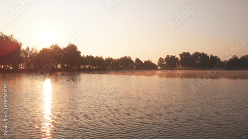 Sun glare on the surface of water. Beautiful trees on the horizon. Picturesque scenery of mountain lake. © DenisProduction.com