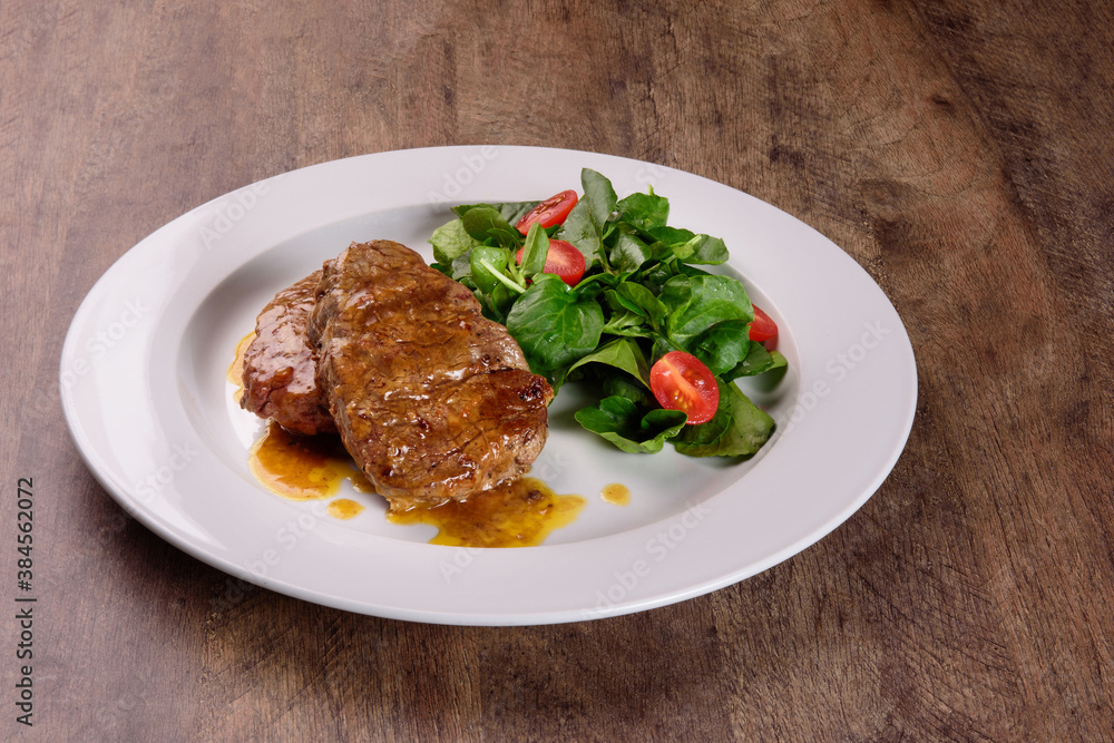 Filet mignon with Demi Glace sauce, watercress salad and cherry tomatoes on a rustic wooden background