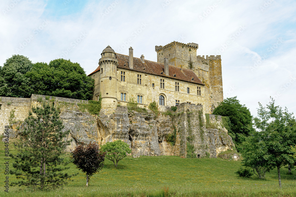 The castle of Excideuil, in the Périgord region of France, is perched on a rocky cliff. The yellow stone contrasts with the blue of the sky.