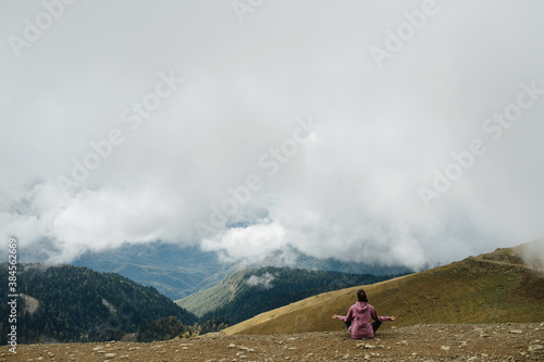 Meditating young woman sitting cross-legged high up in cloudy mountains.