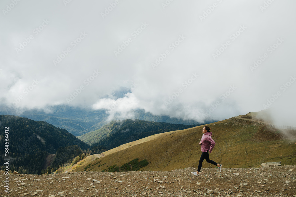 Long shot of young woman running high up in cloudy mountains. Side view.