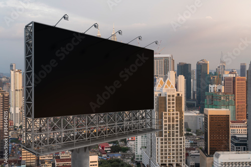 Blank black road billboard with KL cityscape background at sunset. Street advertising poster, mock up, 3D rendering. Side view. The concept of marketing communication to promote or sell idea.