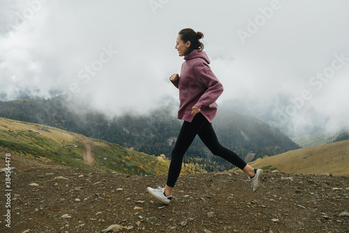 Determined young woman running high up in cloudy mountains. Side view. © zzzdim