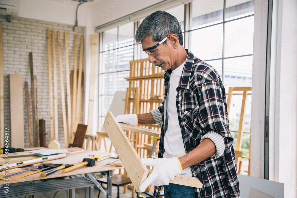 A senior carpenter search and holds examples timber of house wooden interior accessories via laptop for further refinement within a building or condominium. Construction learning concept.