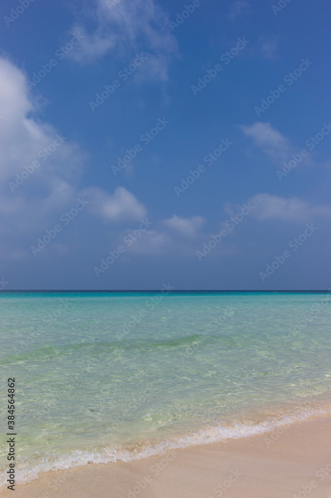 Looking out over a turquoise sea with sandy beach and a blue cloudy sky. Vertical image