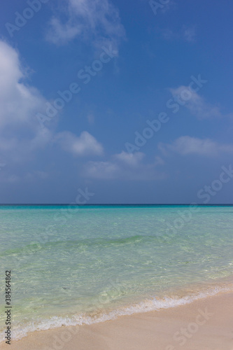 Fototapeta Naklejka Na Ścianę i Meble -  Looking out over a turquoise sea with sandy beach and a blue cloudy sky. Vertical image