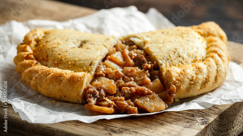 Foto Traditional Cornish pasty filled with beef meat, potato and vegetables on black