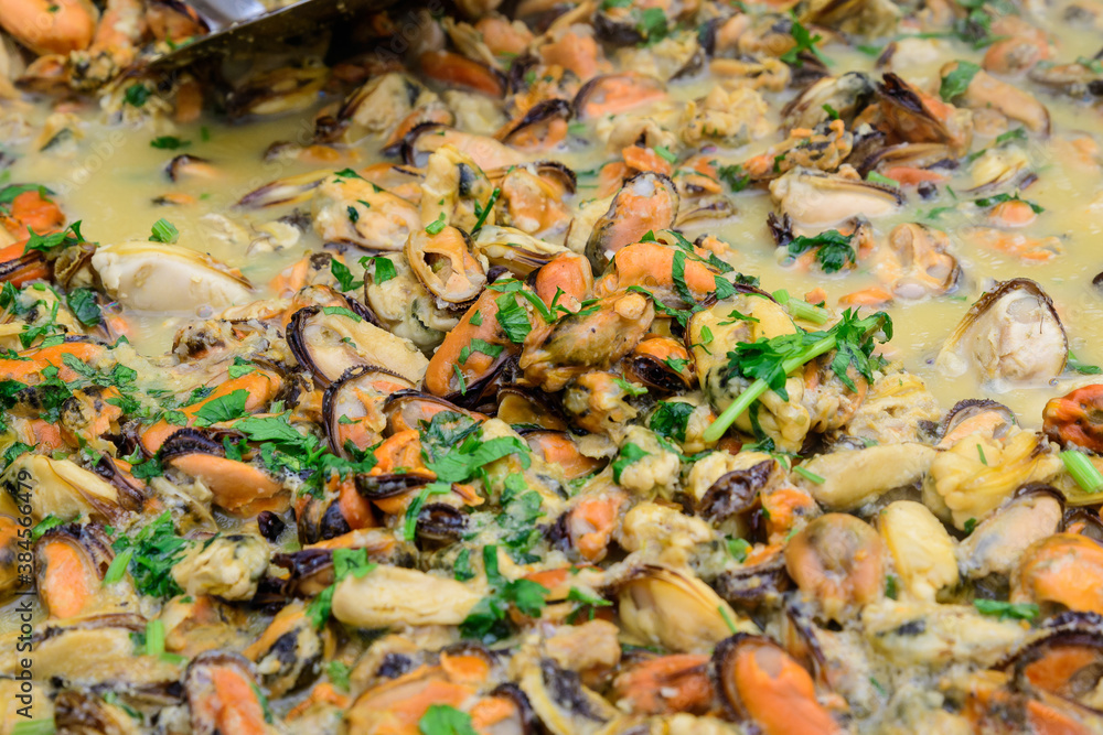 Large group of cooked mussels with tomato and cream sauce at a street food festival, ready to eat seafood,  beautiful orange monochrome outdoor background.