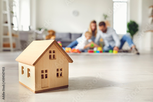 Little wooden house on floor of cozy room with happy family playing in background