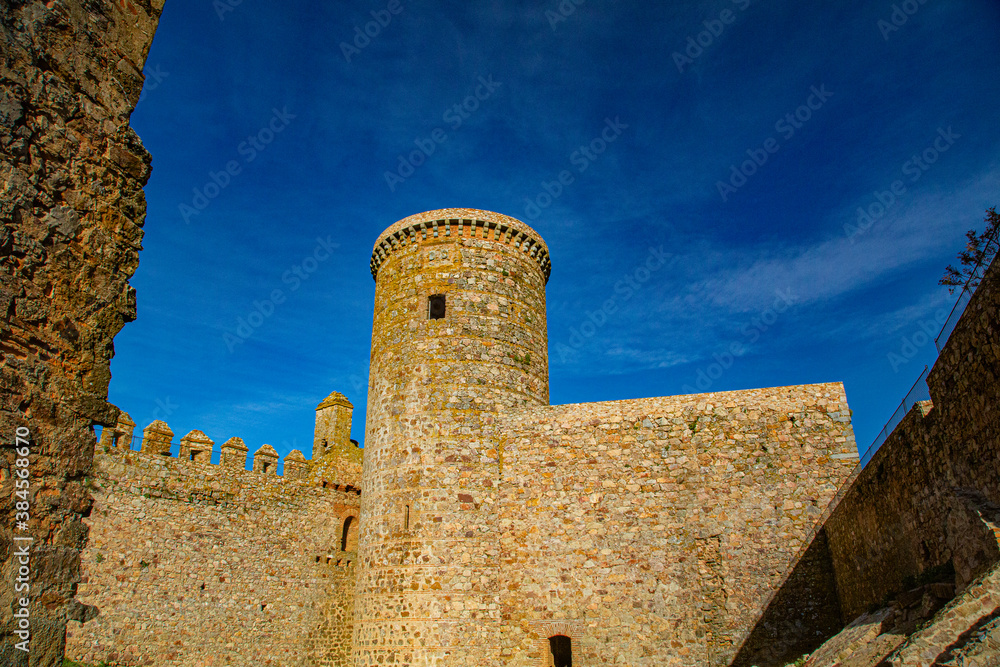 Torre redonda y grandes muros de piedra de castillo con cielo azul intenso